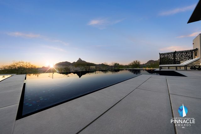 A black negative-edge pool reflecting the sunset sky, with desert mountains on the skyline