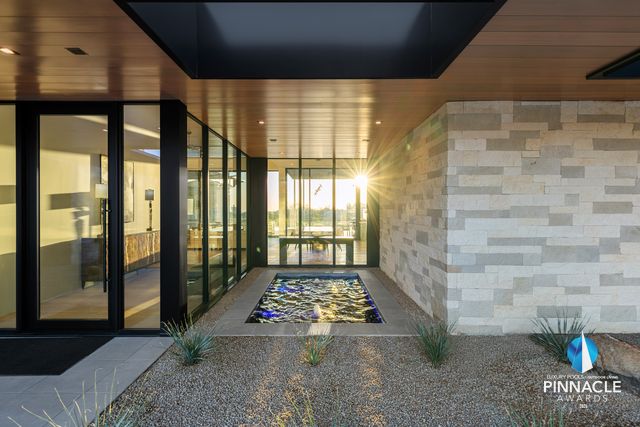 Entry courtyard water feature lit beneath a glass-walled breezeway, framed by stacked-stone walls and desert planting