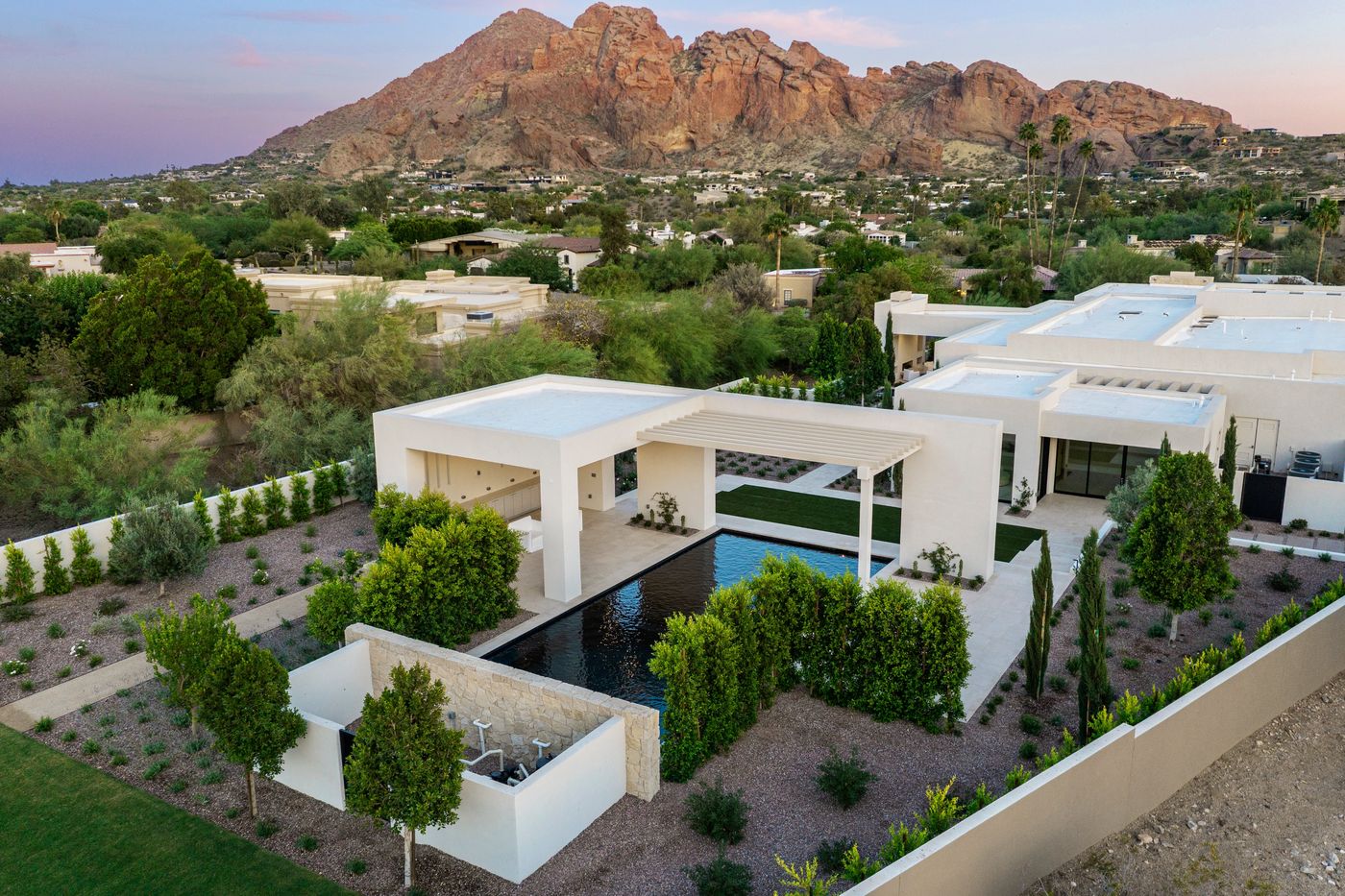 Aerial view of the 2026 PHTA Silver-winning geometric pool by Morris Pools: a long black-bottom pool between a white modern pavilion and pergola, a stacked-stone water wall and a desert mountain behind