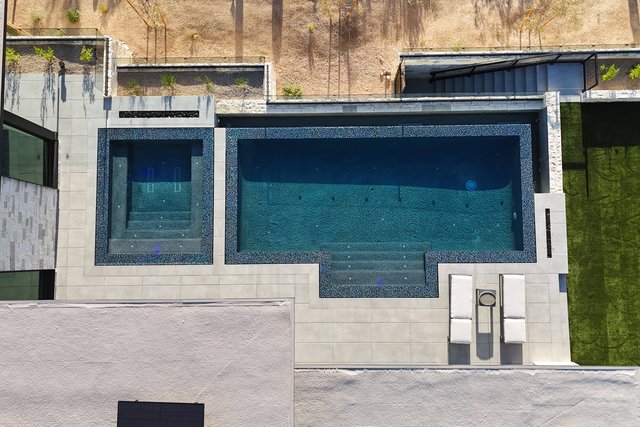 Overhead view of the finished pool and spa with dark glass tile and a sun shelf