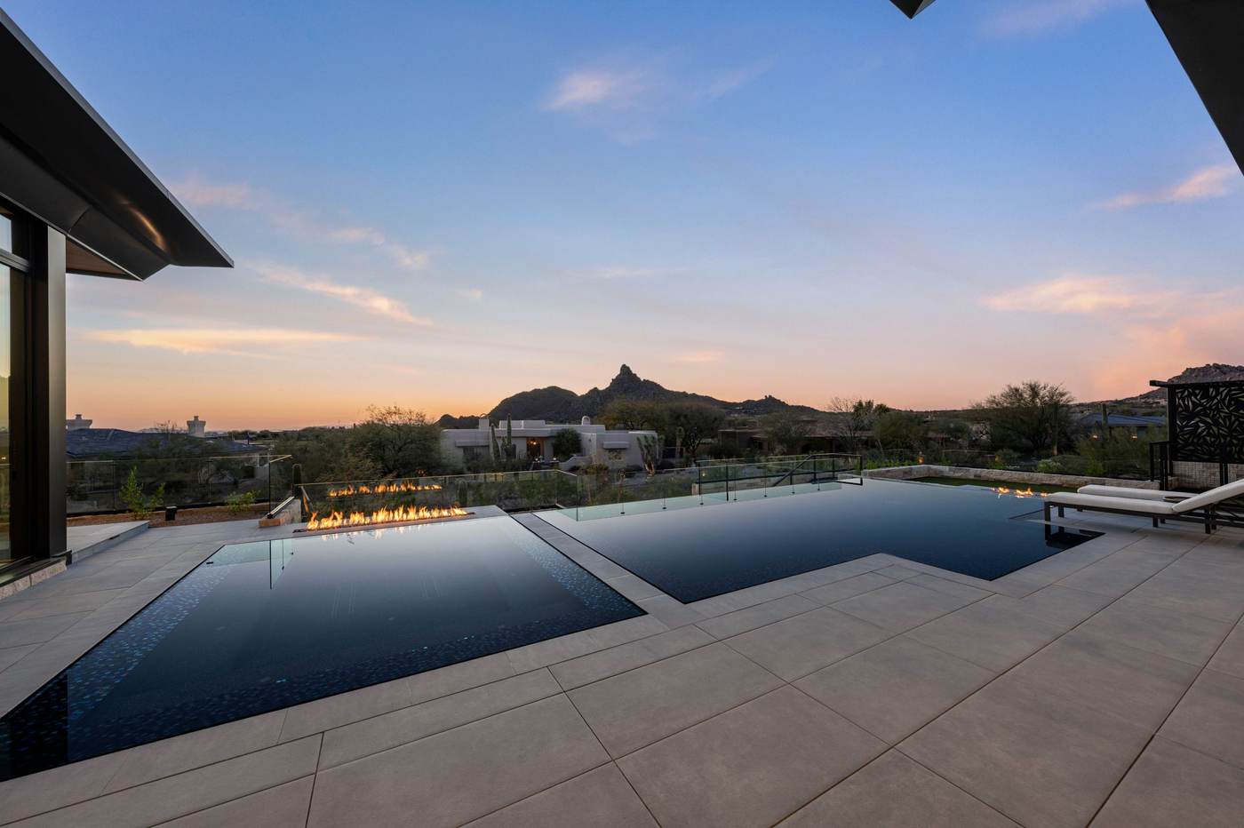 Modern dark-finish infinity-edge pool with linear fire feature and desert mountain view at sunset