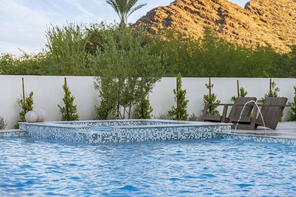 Raised spa spilling into a clear blue pool beneath Camelback Mountain