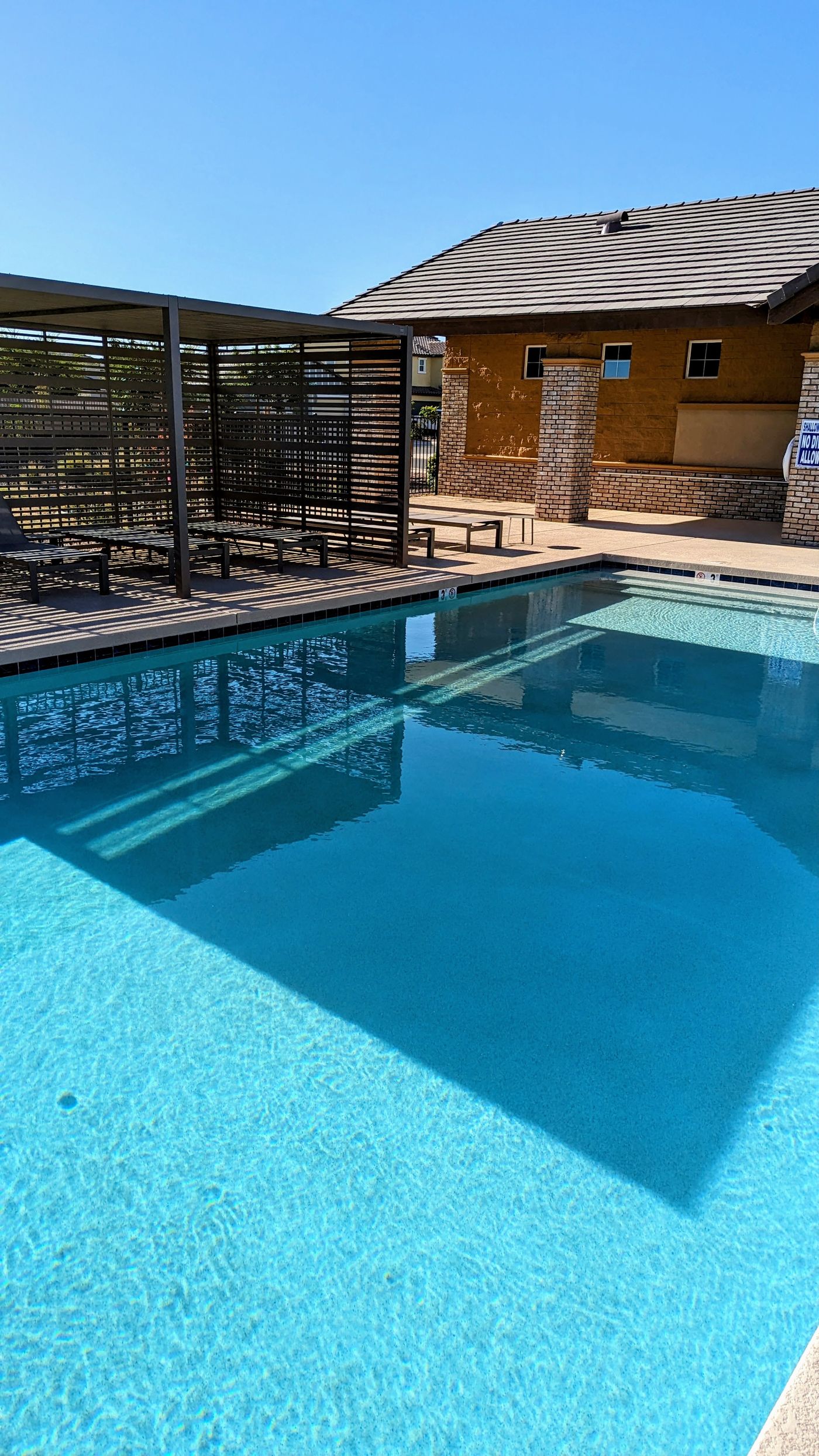 Community pool with a blue tile line, a shade ramada on the deck and homes beyond