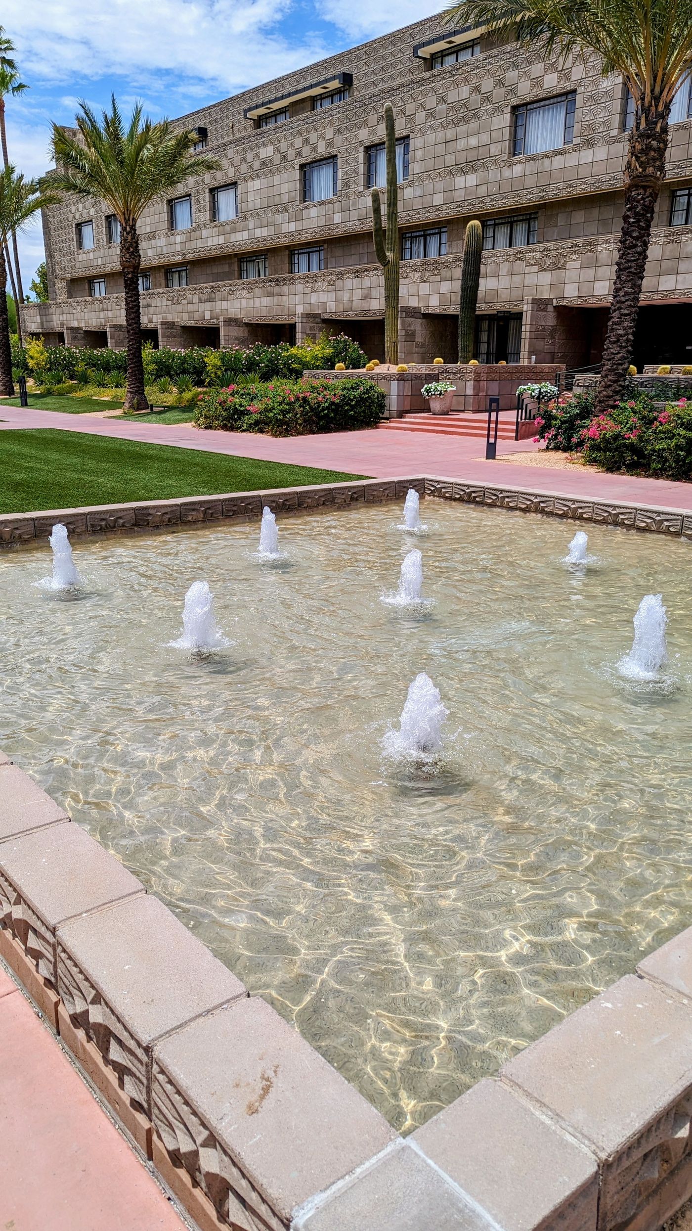 Fountain with rows of bubbling jets in a shallow tiled basin, palms and the resort building behind