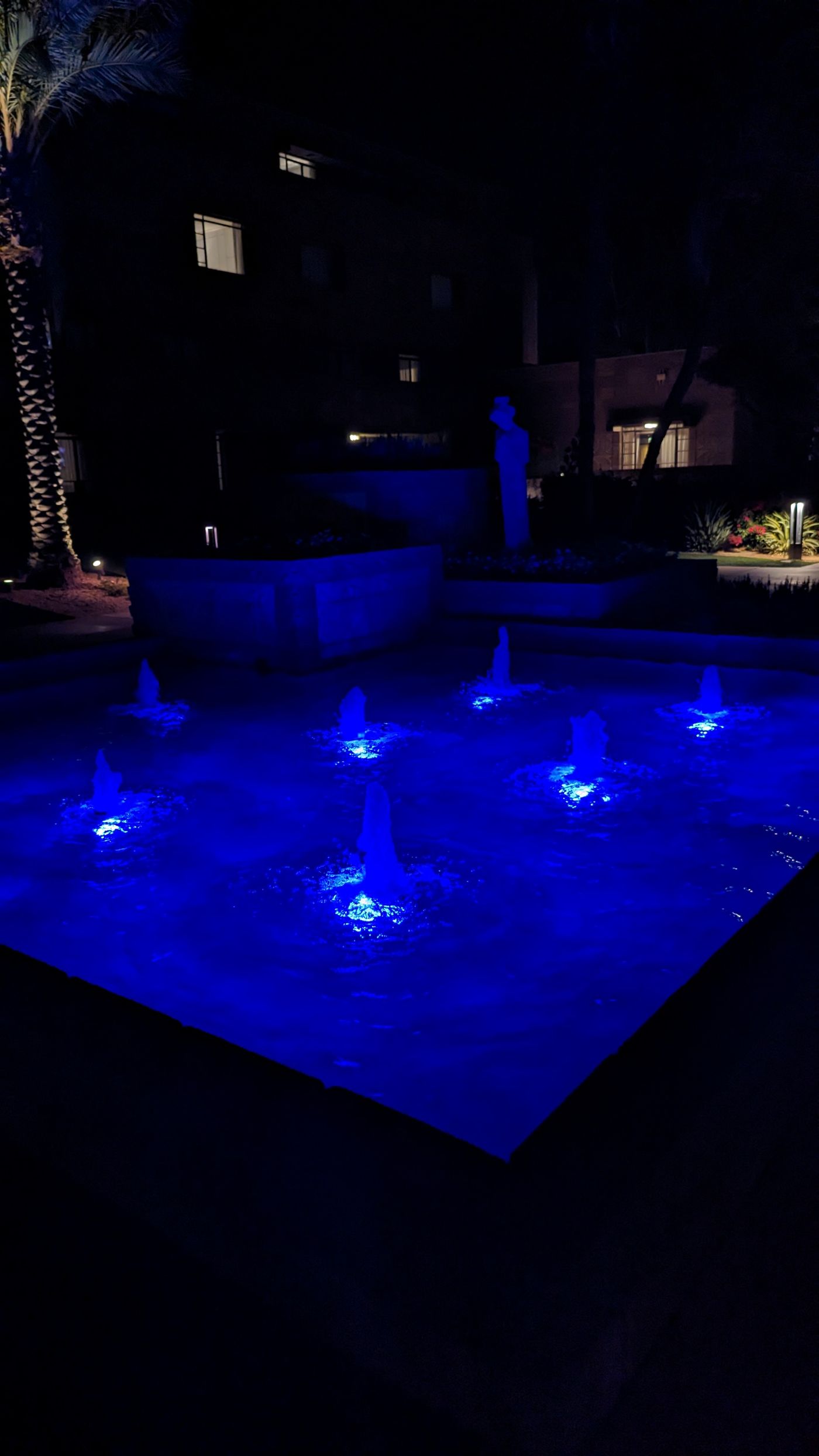 The same fountain at night, its jets lit in blue LED