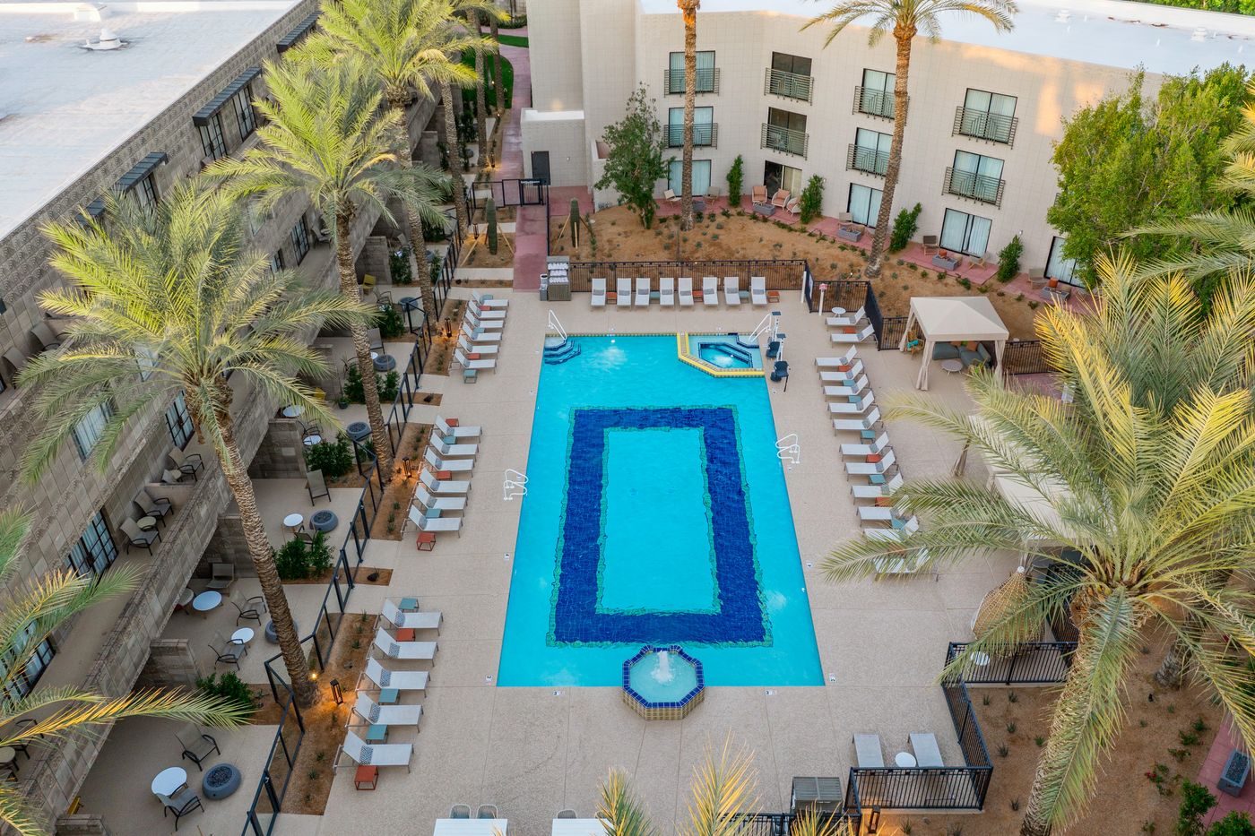 Aerial view of a rectangular resort pool with a deep-blue tile border inlaid in the floor, an octagonal tiled fountain, a spa and rows of loungers