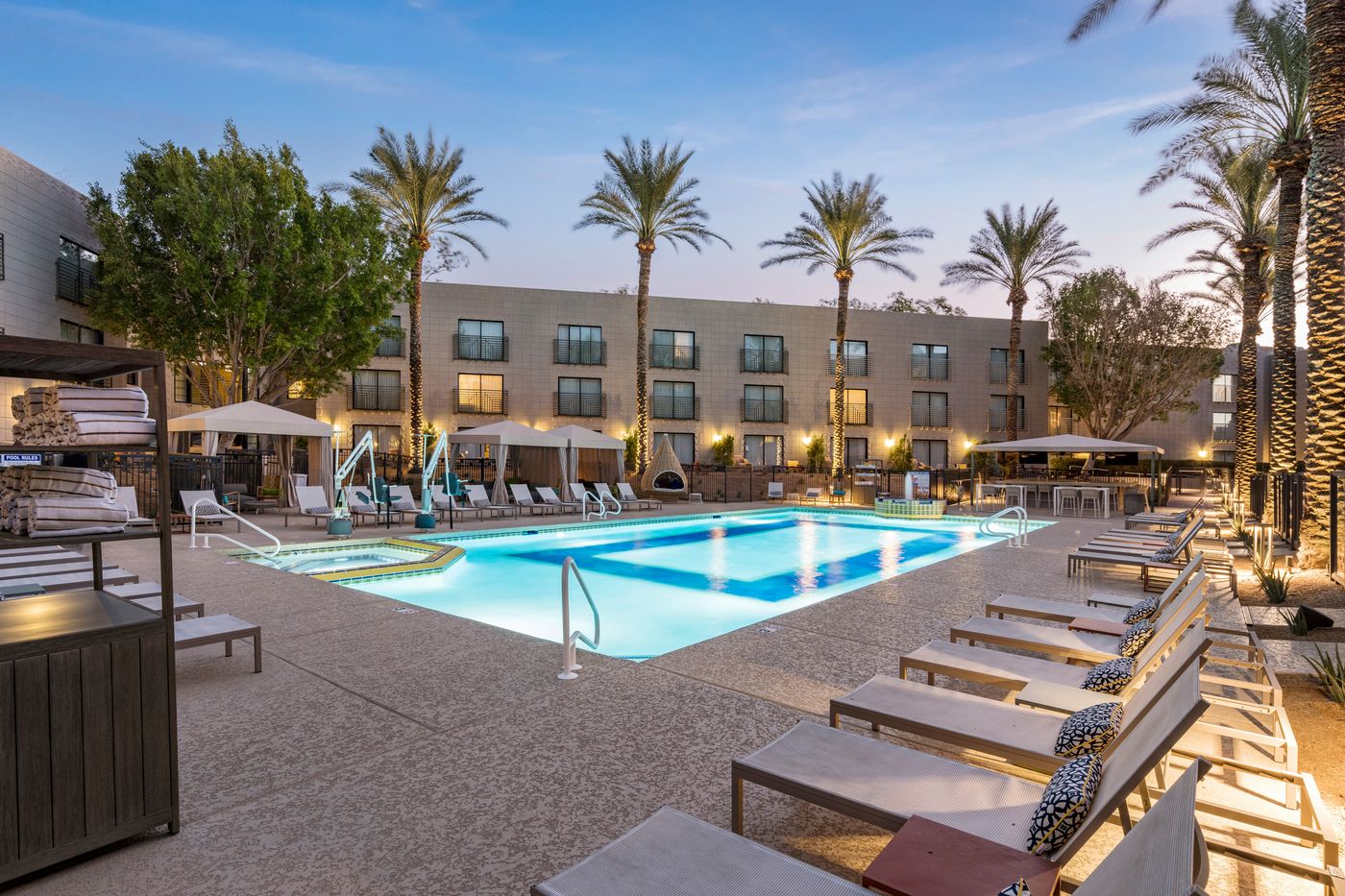 Lit resort pool at dusk with lounge chairs, an adjoining spa and white cabanas
