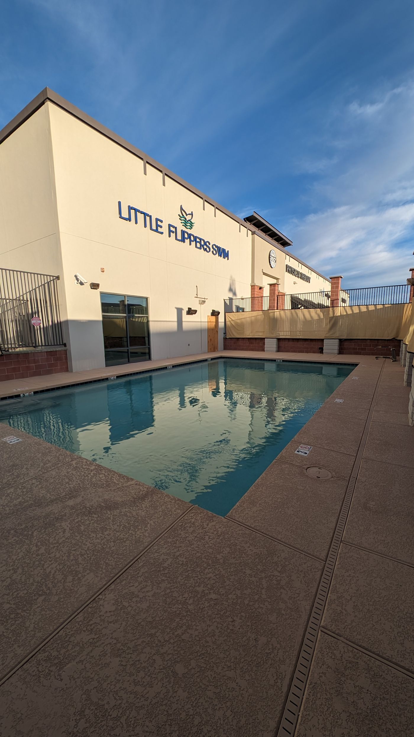 Swim school pool beside a building with a Little Flippers Swim sign, under a blue sky