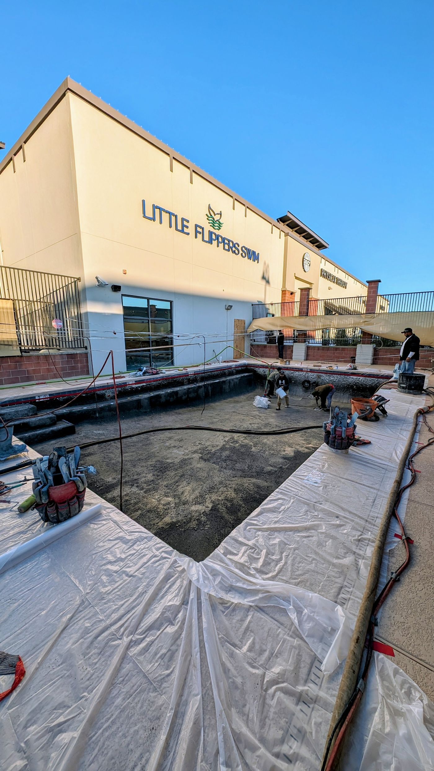 Drained pool mid-remodel with the surrounding deck covered in protective plastic
