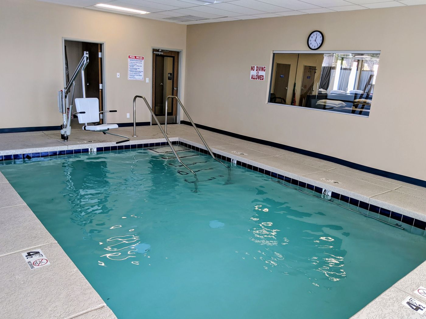 Indoor therapy pool with a blue tile line, stainless grab rails, entry steps and an ADA pool lift at the edge