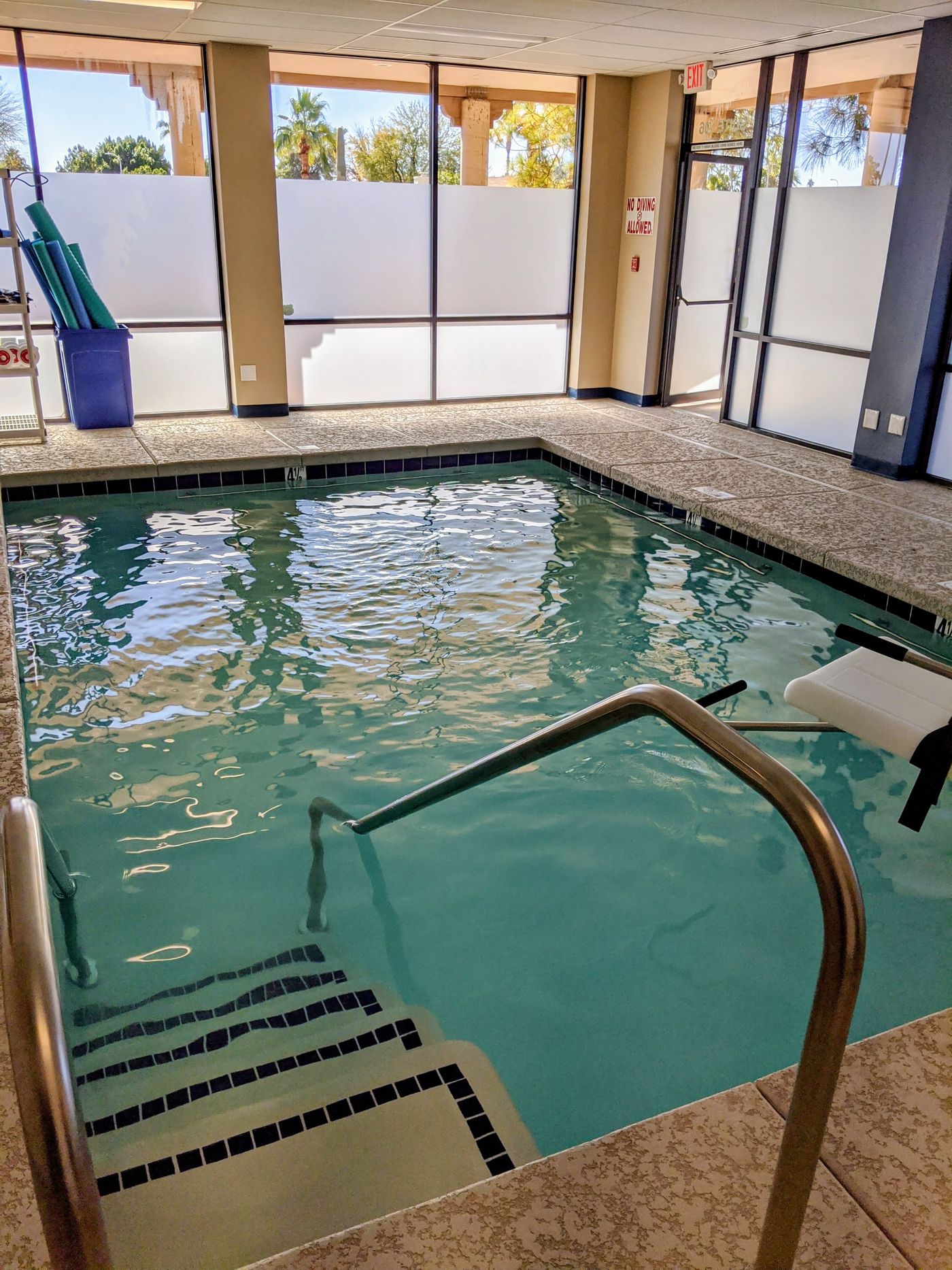 Indoor therapy pool seen from the entry steps and grab rail, with tall windows beyond