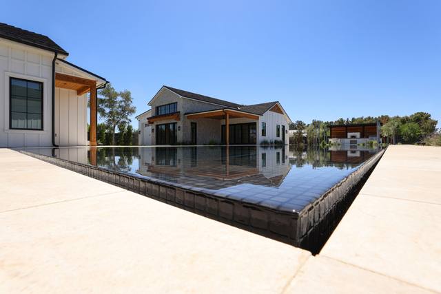 Modern farmhouse with a black-finish perimeter-overflow pool reflecting the house