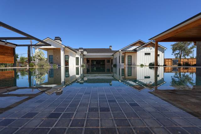 Low-angle view across paver decking to a reflecting pool between two white farmhouse wings
