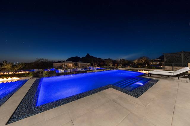 Infinity-edge pool lit blue at dusk with desert mountain silhouettes beyond