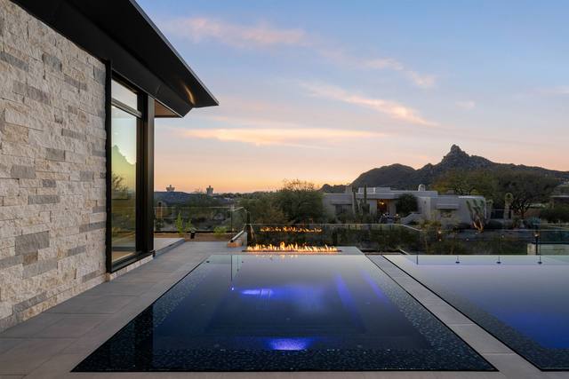 Vanishing-edge pool beside a stone-clad modern home with desert mountain views at sunset