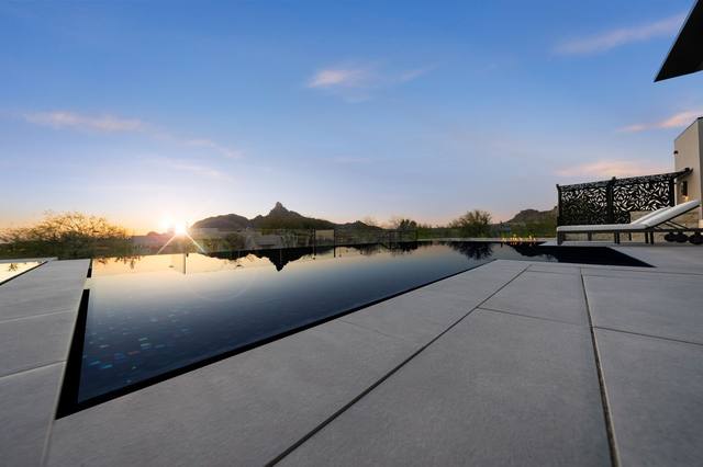 Sunset reflected in a dark vanishing-edge pool with desert mountains on the horizon