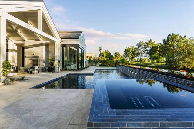 Dark-tiled rectangular pool and raised spa beside a covered patio and modern home
