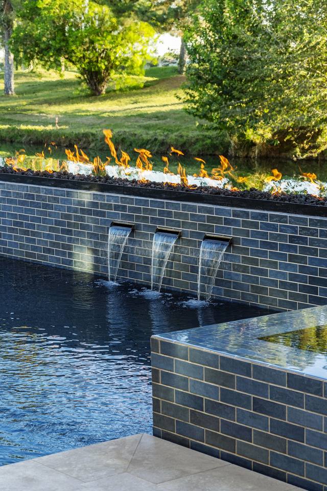 Sheer water descents spilling from a tiled raised wall into a dark pool