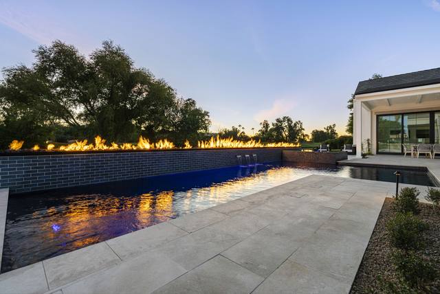 Dark-tiled pool at dusk with a long fire feature running along a raised wall