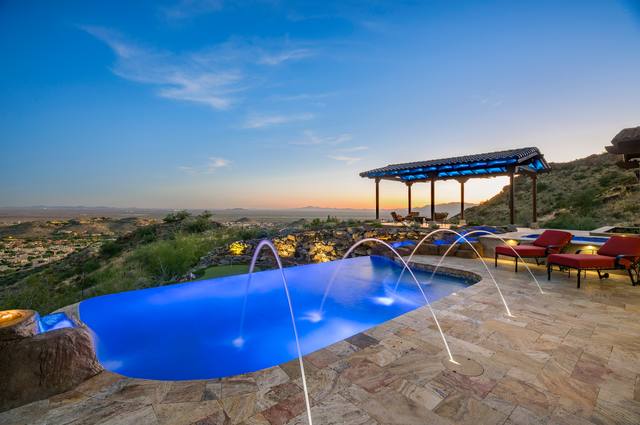 The 2022 PHTA Gold-winning vanishing-edge pool by Morris Pools: hillside pool with arcing deck jets, rock waterfall and pergola at dusk