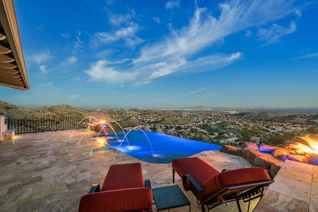 Infinity-edge pool with laminar deck jets, fire feature and panoramic valley view at dusk