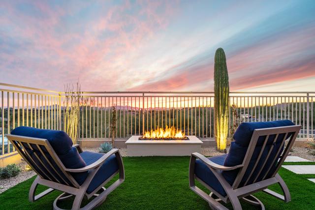 Two lounge chairs facing a fire table on artificial turf at sunset with a saguaro nearby