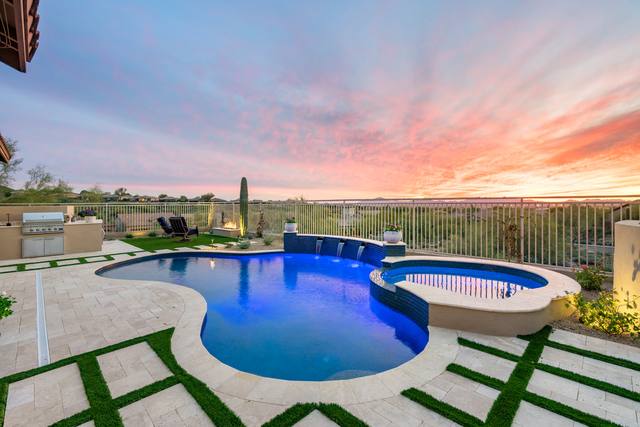 Freeform pool and raised spa at sunset with turf strips set into the pavers