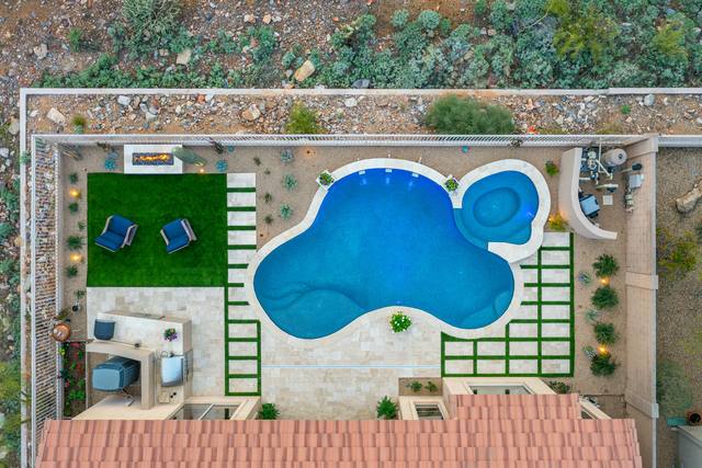 Aerial view of a freeform pool and spa with turf-and-paver patterns and a fire pit seating area