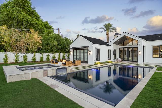 Dark-finish pool and spa along a lawn with a white modern farmhouse behind