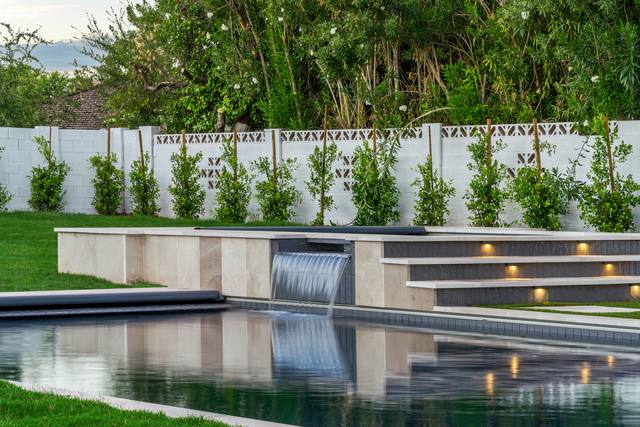 Sheer descent from a raised stone ledge into a reflecting pool along a hedge-lined wall
