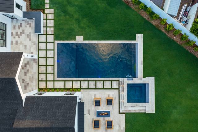 Aerial view of a rectangular pool and spa with paver-and-turf patio and fire pit