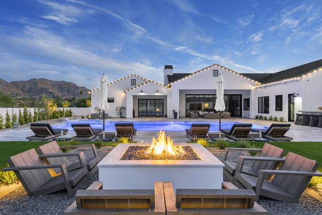 Fire pit lounge with Adirondack chairs in front of a lit pool and white farmhouse