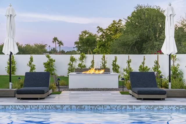 Pool with glass-tile waterline, fire table and two chaise loungers under umbrellas