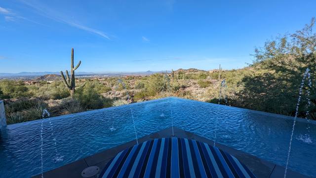 Infinity-edge pool with deck jets overlooking desert saguaros and mountains