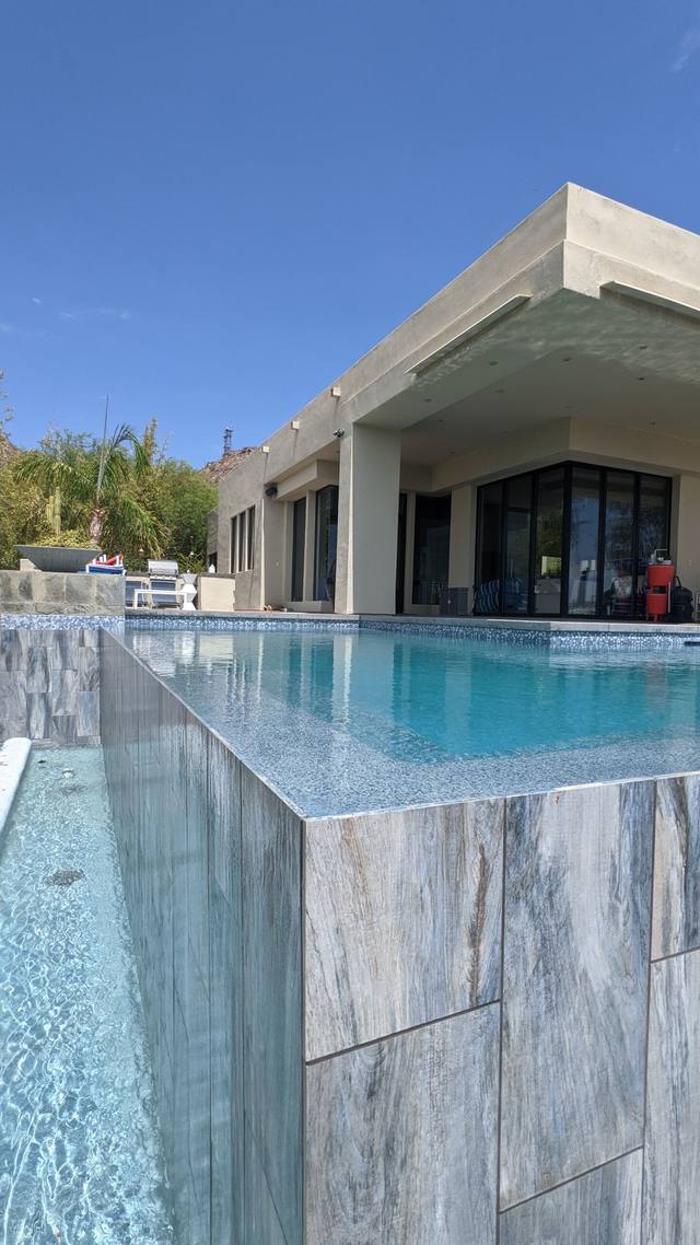 Knife-edge vanishing pool with marble-look tile beside a modern home