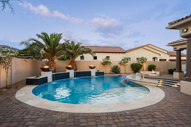 Freeform pool with fire bowls, sheer descents, raised spa and fire pit in a Spanish-style backyard