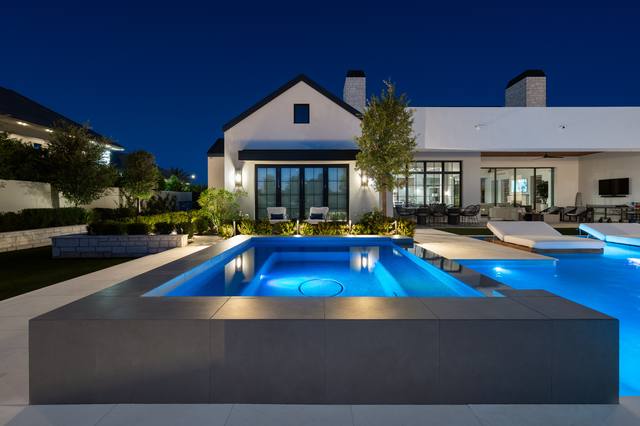 Raised spa with a sheer descent beside a pool and a white farmhouse at night