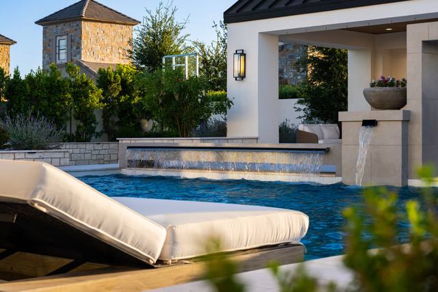 Close-up of a sheer-descent water feature and a bowl scupper pouring into the pool, with a lounger in the foreground