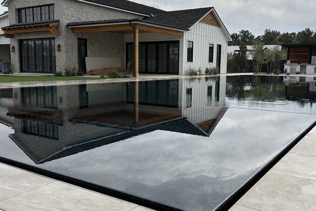 A 2025 PHTA Bronze-winning vanishing-edge pool by Morris Pools: black-tile pool with a knife edge mirroring a modern farmhouse